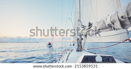 Sloop rigged yachts sailing in a still water at sunset. Frost and first snow on the deck, close-up view to the bow, mast, ropes and sails. Clear blue sky with colorful winter clouds. Norway Royalty-Free Stock Photo #2153859531