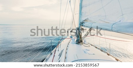 White sloop rigged yacht sailing at sunset. Clear sky after the storm. View from the deck to the bow, mast, sails. Transportation, travel, cruise, sport, recreation, leisure activity, racing, regatta Royalty-Free Stock Photo #2153859567