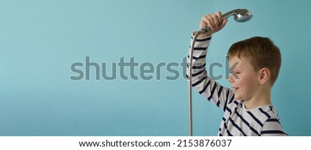 Banner whith a happy smiling boy with a watering can from the shower over his head on a blue background. The concept of housewarming, renovation, happy childhood. Place fo text. Royalty-Free Stock Photo #2153876037
