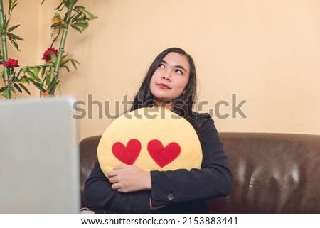 A young woman hugging an emoji stuffed toy, thinking about her love ones, motivating her to work harder.