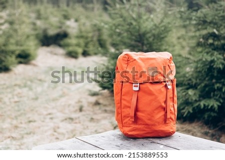 Hipster orange backpack. View from front tourist traveler bag with forest background. Travel outdoor concept