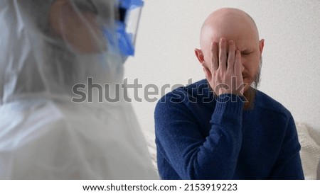 A sick man complains to the doctor about his health, the Man coughs and says that his throat hurts. A doctor in a protective suit, mask and goggles writes down the symptoms of the disease.
