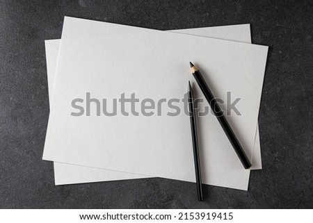 Paper mockup. Watercolor A4 paper with black pencils on dark background. Top view. Can be used as a template for drawings. Royalty-Free Stock Photo #2153919415