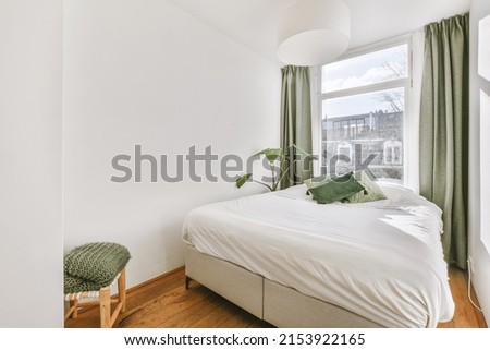 Comfortable bed and chair placed in small narrow minimalist style bedroom with white walls and green curtains on window in modern apartment Royalty-Free Stock Photo #2153922165