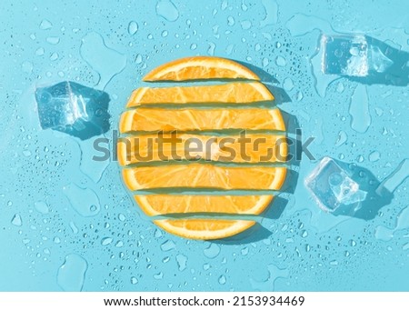 Orange fruit slices with melting ice cubes on blue background. Minimal citrus fruits concept. Creative summer refreshing food layout. Trendy vacation aesthetic. Flat lay with sunshine shadows. Royalty-Free Stock Photo #2153934469