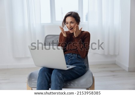 Excited cheerful happy enthusiastic shocked curly awesome young woman talks with friend in video conference call tells about latest cool news holds laptop raise hand active gesturing in chair at home Royalty-Free Stock Photo #2153958385