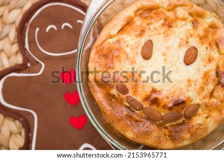 Freshly baked apple pie with almond nuts in the form of a smile in a glass dish on a wicker background with a stick in the form of a gingerbread.