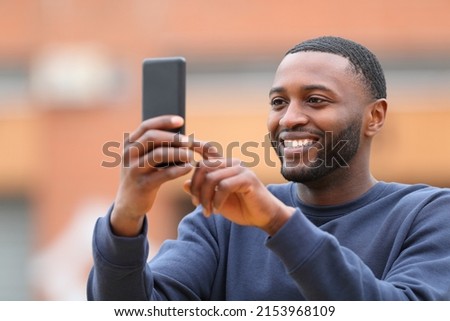 Happy man with black skin taking selfie or photo with smart phone standing in the street