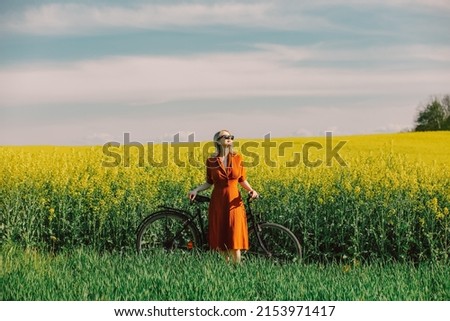 Beautiful blond girl in vintage dress and sunglasses with bicycle in rapeseed field in spring