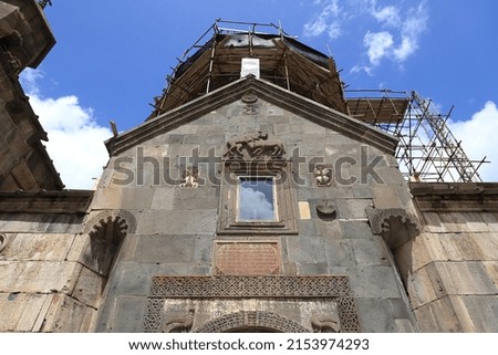 The facades of the ancient monastery of Geghard in the mountains of Armenia - built into the rock - against the backdrop of a blue sky with clouds.
