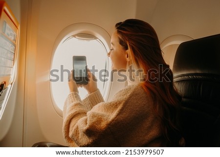 The girl sits on the plane and takes a photo on the phone. Travel.