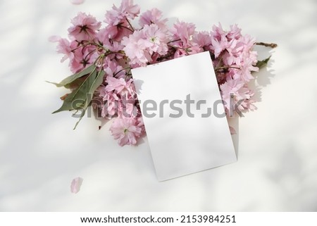 Wedding spring styled stock photo. Feminine desktop. Blossoming pink Japanese cherry tree, sakura branch. Blank greeting card, invitation mockup in sunlight. White dappled table background, top view.