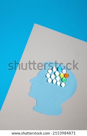 paper head on a blue background with a brain of abstract beads, a few colorful creative creating ideas in the brain