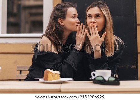 Gossiping. Two beautiful young women gossiping telling something on ear while sitting in the cafe. Communication and friendship concept. Young woman telling her friend some secrets. Royalty-Free Stock Photo #2153986929