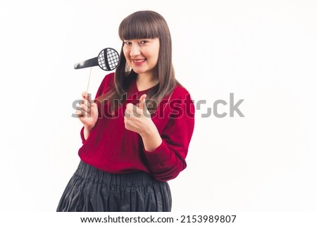 young woman with dark straight hair having fake props microphone on a stick and showing thumb up white background isolated copy space studio shot . High quality photo