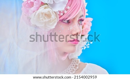 Beauty, makeup and hairstyle. Portrait of a pretty teen girl with bright pink make-up posing in colored pink wig and flower wreath on head. Studio portrait on a blue background.