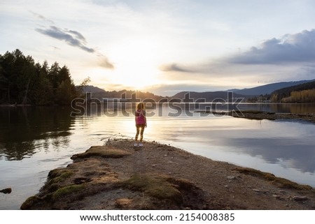 Adventurous Woman on a shore enjoying colorful Sunset. Shoreline Trail, Port Moody, Greater Vancouver, British Columbia, Canada. Park in Modern City. Royalty-Free Stock Photo #2154008385