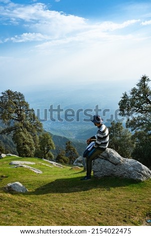 Moment of loneliness. Man sit on the peak of rock and watching into colorful mist and fog in forest valley. Man hiking. Sad person relaxing. Spring nature. Tired man relaxing in Triund trek, Himachal.