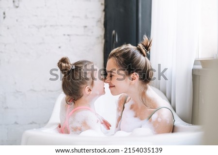Young mother woman and little tween girl daughter having fun in bath with foam at home