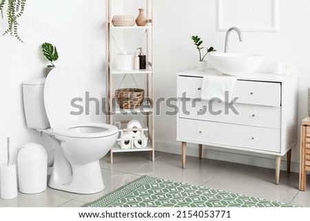 Interior of white restroom with toilet bowl and chest of drawers Royalty-Free Stock Photo #2154053771