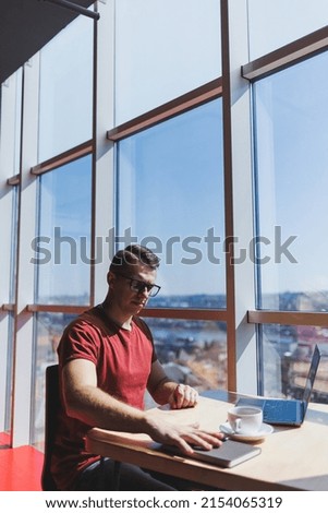 Smart software developer sitting at desktop in coworking space with laptop and creating publishing idea, using netbook for messaging and networking during freelance work