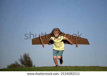 Child playing with cardboard toy wings in the park. Concept of children day. Kid boy in an pilot costume is playing and dreaming of becoming a aviator spaceman. Kids freedom concept. Royalty-Free Stock Photo #2154082511