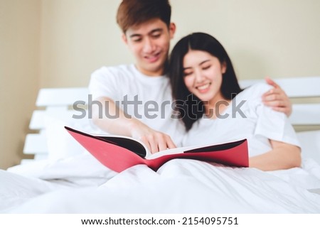 asian couples planning for future looking books, buying life insurance, buying houses, looking at wedding photos.