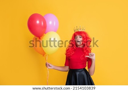 surprised child in crown with party balloon on yellow background