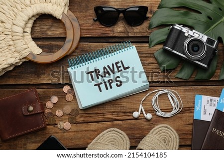 Notebook with phrase Travel Tips and tourist items on wooden table, flat lay