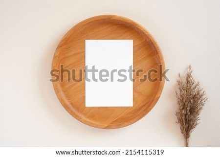 Blank paper sheet on wooden plate, pastel beige background. Card mockup. Elegant wedding layout. Bouquet of dried flowers pampas grass. Minimal eco template Soft shadow. Aesthetic interior, White page