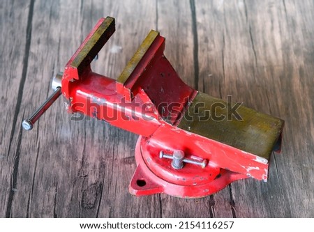 old red bench vise on wooden table, a clamb as fastening device 