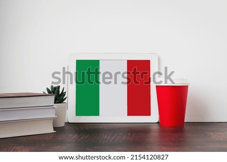 National flag of Italia on the tablet, textbooks, a red cup of hot drink coffee or tea on the table, the concept of learning italian