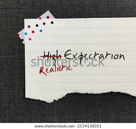 Stick note with handwritten HIGH EXPECTATION crossed HIGH off, replaced with REALISTIC, to be able to move forward in life with more acceptance when things turn out lower than expected Royalty-Free Stock Photo #2154136011