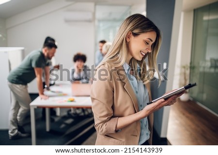Beautiful young woman team leader posing with confident expression as her colleagues hold a meeting in background. Positive woman with coworkers in conference room.