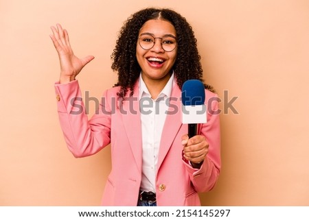 Young African American TV presenter woman isolated on beige background receiving a pleasant surprise, excited and raising hands.