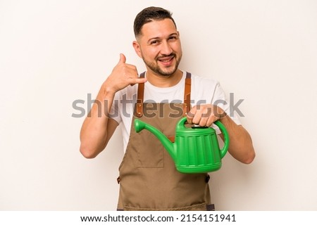 Gardener hispanic man holding a watering can isolated on white background showing a mobile phone call gesture with fingers.