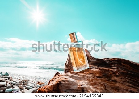 Toilet water. A rectangular glass bottle of golden perfume standing on a driftwood. Ocean waves and sunny sky in the background. Low angle view. Perfume concept and advertising template. Royalty-Free Stock Photo #2154155345