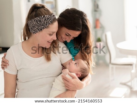 A lesbian couple smiling at their baby, gay marriage, gay parents and adoption concept Royalty-Free Stock Photo #2154160553
