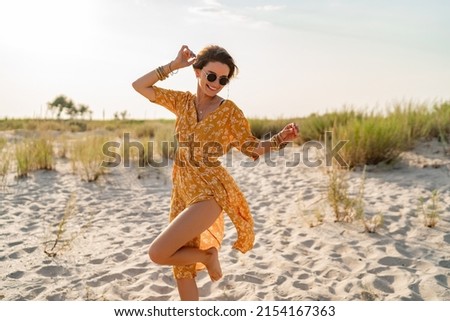 stylish attractive slim smiling woman on beach in summer style fashion trend outfit carefree and happy, feeling freedom, wearing yellow printed dress boho style chic and sunglasses Royalty-Free Stock Photo #2154167363