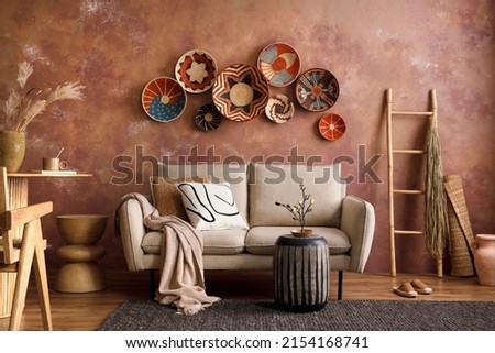 The stylish boho composition at living room interior with design beige sofa, coffee table, wicker baskets and elegant personal accessories. Brown and white pillows and plaid Cozy apartment. Home decor Royalty-Free Stock Photo #2154168741