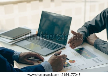 Close-up of two businessmen with pens pointing to graphs while chatting on wooden table with laptop, teamwork discussing up and down financial accounts, market economy.