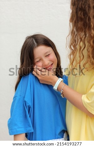 happy woman and child girl 9-11 years old having fun together. young woman in yellow t shirt is touching face her smiling daughter in blue t shirt on white background. mothers day, love family concept