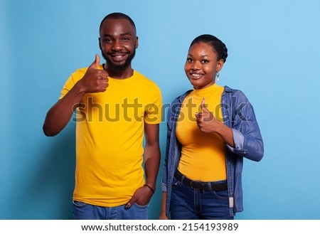 Optimistic partners showing thumbs up sign to agree, standing over blue background. Positive man and woman doing okay gesture with hands, feeling confident about successful choice. Royalty-Free Stock Photo #2154193989