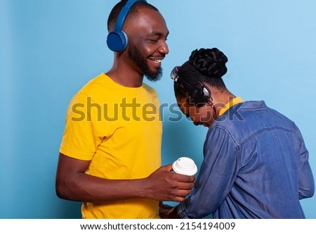 Man and woman laughing and listening to music on headphones in studio. Playful couple enjoying playlist song on headset, feeling happy together. Girlfriend and boyfriend having fun with audio