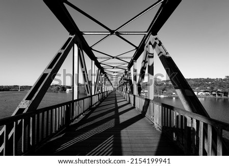 Old steel bridge over Ruhr river at “Baldeneysee“ in Essen Germany. Former railway bridge with symmetric rivet construction today is for pedestrians and bikers. Black and white greyscale, wide angle. Royalty-Free Stock Photo #2154199941