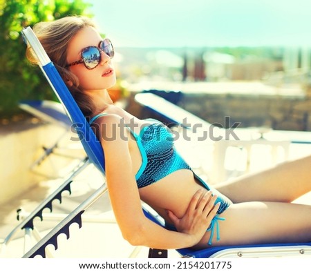 Summer vacation, beautiful relaxing young woman lying on deckchair wearing swimsuit on pool background