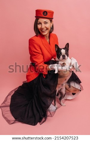 Smiling young caucasian woman spending time with her pet in studio on pink background. Brunette girl posing with black and white dog. Concept of friendship between man and animals.
