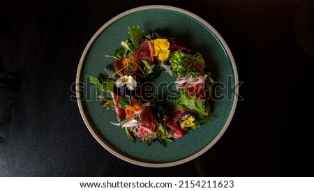 Top view of Tartare beef flower circle salad in the fine dining Japanese restaurant, with a green round plate in black scene reflection table background, raw beef, onion, salad, carrot, flowers Royalty-Free Stock Photo #2154211623
