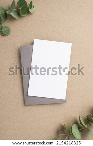 Business concept. Top view vertical photo of paper sheet grey envelope and eucalyptus on beige background with blank space