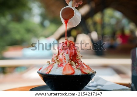 Japanese shaved ice dessert , Hand pouring sweet strawberry sauce on ice cream. Served with strawberry kakigori bingsu topped with almond stick condensed milk. Traditional summer dessert in Japan. Royalty-Free Stock Photo #2154217147